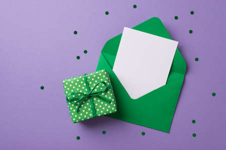 Top view photo of st patricks day decor confetti green envelope with paper sheet and green giftbox with polka dot pattern on isolated pastel violet background with blank spaceの写真素材