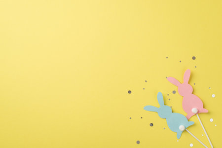 Top view of two rabbits pink and blue one with confetti on the isolated yellow background copyspaceの写真素材