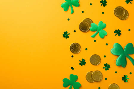 Top view photo of st patrick's day decorations green shamrocks clover shaped confetti and gold coins on isolated yellow background with copyspaceの写真素材