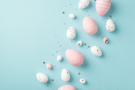 Top view photo of easter decorations glowing confetti pink and white easter eggs on isolated pastel blue background with copyspaceの写真素材