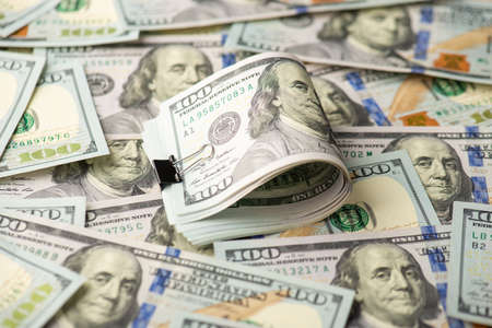 Photo of pile of one hundred dollar bills with black binder clip and dollar banknotes