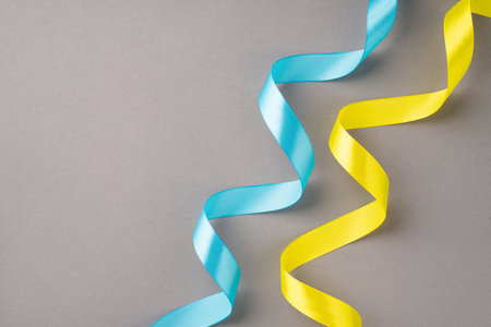 Stop the war in Ukraine concept. Top view photo of national flag colors yellow and blue wavy ribbons on isolated gray background with copyspaceの写真素材