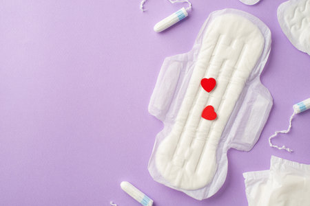 Top view photo of tampons and sanitary napkin with red hearts on isolated pastel lilac background with copyspaceの写真素材