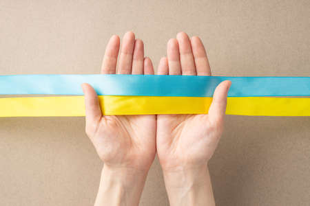 Stop the war in Ukraine concept. Top overhead view photo of female hands holding national flag on beige backgroundの写真素材
