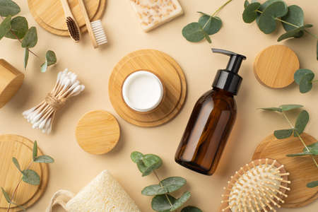 Eco cosmetic concept. Top view photo of glass dispenser bottle cream jar soap hair brush eucalyptus cotton buds toothbrushes and wooden stands on isolated beige backgroundの写真素材