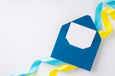 Stop the war in Ukraine concept. Top view photo of open blue envelope with letter over national flag colors yellow and blue curly ribbons on isolated white background with blank spaceの写真素材