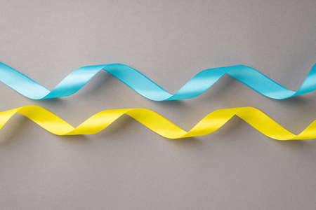 Stop the war in Ukraine concept. Top view photo of national flag colors yellow and blue wavy ribbons on isolated gray backgroundの写真素材