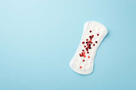 Top view photo of panty liner with red heart shaped confetti on isolated pastel blue backgroundの写真素材