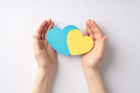 Stop the war in Ukraine concept. First person top view photo of female hands giving two yellow and blue hearts on white backgroundの写真素材