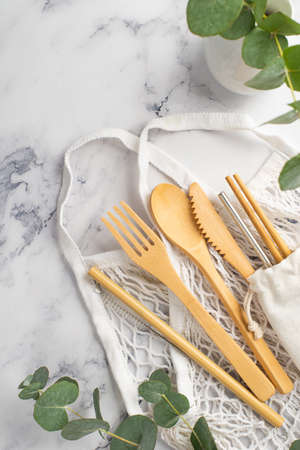no plastic concept. Top view vertical photo of wooden cutlery fork spoon knife chopsticks white string bag steel straw cleaning brush and vase with eucalyptus on white marble backgroundの写真素材