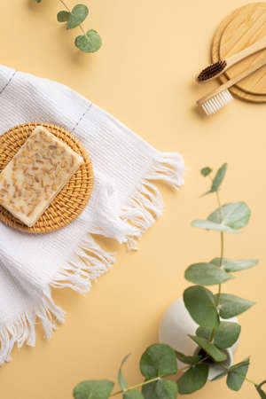 Top view vertical photo of ceramic vase with eucalyptus white towel toothbrushes and soap on wicker stands on isolated pastel beige backgroundの写真素材