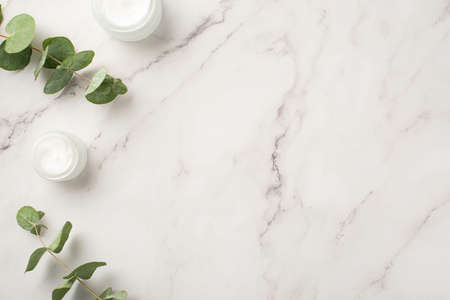 Skin care cosmetics concept. Top view photo of cream bottles and eucalyptus on white marble background with blank spaceの写真素材