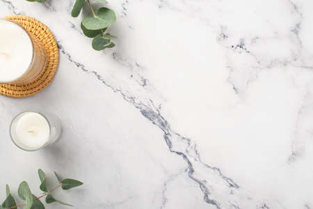 Top view photo of candles on rattan serving mat and eucalyptus on white marble background with copyspaceの写真素材