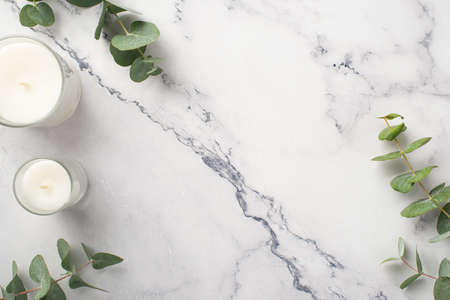 Top view photo of candles with glass holders and eucalyptus on white marble background with copyspaceの写真素材