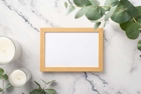 Top view photo of wooden photo frame candles and eucalyptus on white marble background with empty spaceの写真素材