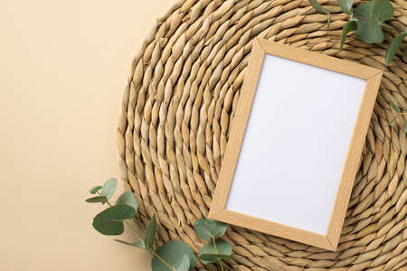 Top view photo of wooden photo frame eucalyptus sprigs and decorative placemat on isolated beige background with copyspaceの写真素材