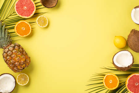 summer concept. Top view photo of tropical fruits cracked coconuts cut oranges lemons grapefruits pineapple and palm leaves on isolated yellow background with copyspaceの写真素材