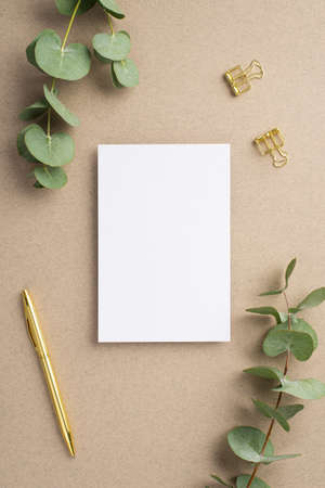 Top view vertical photo of paper card gold pen binder clips and eucalyptus on beige background with empty spaceの写真素材
