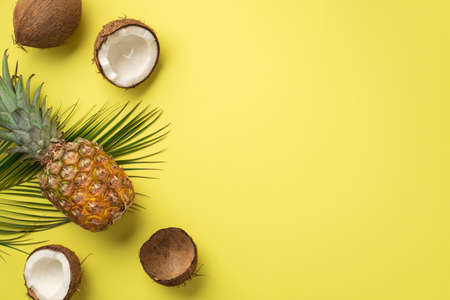summer concept. Top view photo of tropical fruits pineapple cracked coconuts and green palm leaves...