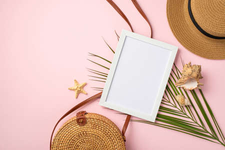 Summer weekend concept. Top view photo of white photo frame shells starfish hat round rattan bag and palm leaves on isolated pastel pink background with empty spaceの写真素材