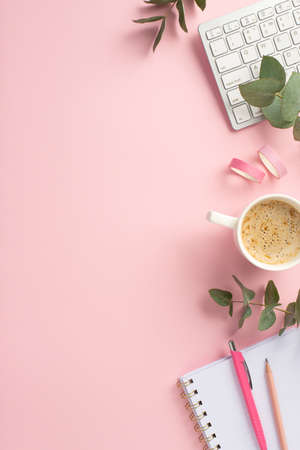 business concept. Top view vertical photo of workstation keyboard cup of hot drinking pens open notebook adhesive tape and eucalyptus on isolated pink background with empty spaceの写真素材