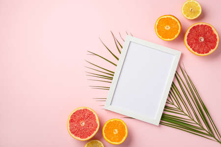 Summer weekend concept. Top view photo of white photo frame and ripe tropical fruits cut lemon...