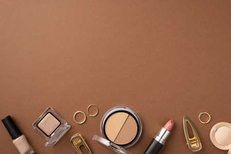 Make up beauty concept. Top view photo of eyeshadow nail polish contouring palette gold rings barrettes and lipstick on isolated brown background with empty spaceの写真素材