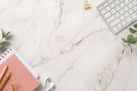 business concept. Top view photo of workstation keyboard pink organizers wireless earbuds pens gold binder clips and eucalyptus branches on white marble background with blank spaceの写真素材