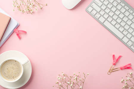 business concept. Top view photo of keyboard computer mouse notepads cup of coffee on saucer clips and white gypsophila flowers on isolated pastel pink background with empty space in the middleの写真素材