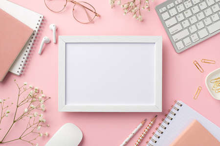 business concept. Top view photo of workplace photo frame keyboard computer mouse notebooks clips pencils glasses earbuds white gypsophila flowers on isolated pastel pink background with copyspaceの写真素材