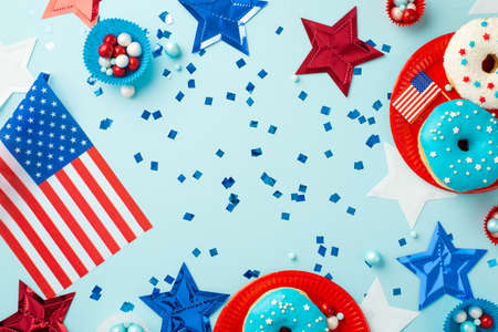 Fourth of July concept. Top view photo of national flags stars confetti paper backing molds with candies and plates with glazed donuts on isolated pastel blue backgroundの写真素材