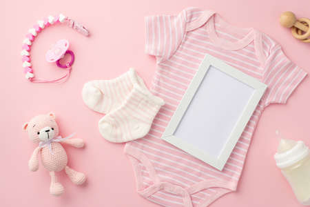baby concept. Top view photo of photo frame pink infant clothes bodysuit socks baby's dummy chain bottle wooden rattle and knitted teddy-bear toy on isolated pastel pink background with empty spaceの写真素材