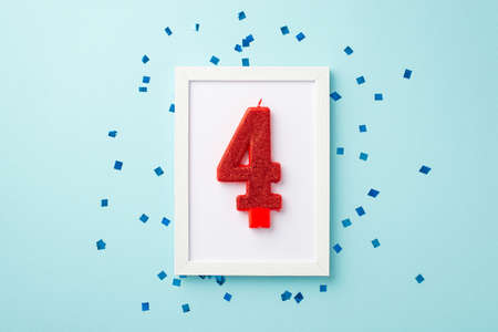 USA Independence Day concept. Top view photo of photo frame with number 4 candle and confetti on isolated pastel blue backgroundの写真素材