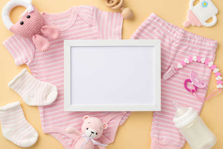 baby concept. Top view photo of photo frame pink shirt panties socks pacifier chain knitted bunny rattle toy teddy bear bottle and teether on isolated pastel beige background with empty spaceの写真素材