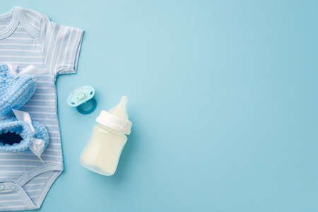 baby boy concept. Top view photo of blue infant clothes bodysuit knitted booties soother and milk bottle on isolated pastel blue background with copyspaceの写真素材