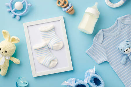 baby accessories concept. Top view photo of photo frame with socks knitted bunny and bear toys blue shirt milk bottle teether rattle booties and soother on isolated pastel blue backgroundの写真素材