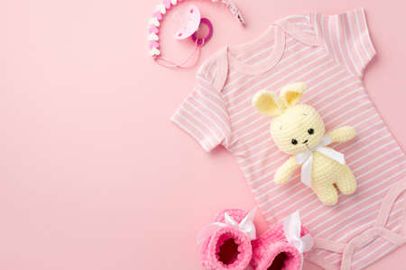 baby accessories concept. Top view photo of pink infant clothes bodysuit booties pacifier chain and knitted bunny toy on isolated pastel pink background with empty spaceの写真素材
