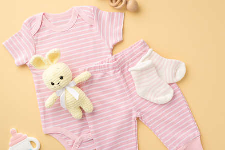 baby accessories concept. Top view photo of pink bodysuit panties socks knitted bunny toy bottle shaped teether and wooden rattle on isolated pastel beige backgroundの写真素材