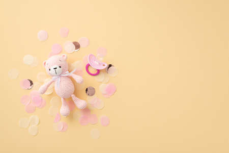baby accessories concept. Top view photo of pink knitted teddy-bear toy soother and shiny confetti on isolated pastel beige backgroundの写真素材
