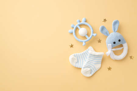 baby accessories concept. Top view photo of blue teether knitted bunny rattle toy tiny socks and gold stars on isolated pastel beige background with copyspaceの写真素材