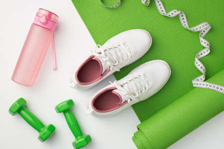 fitness accessories concept. Top view photo of white sports shoes pink bottle of water green sports mat dumbbells and tape measure on isolated white backgroundの写真素材