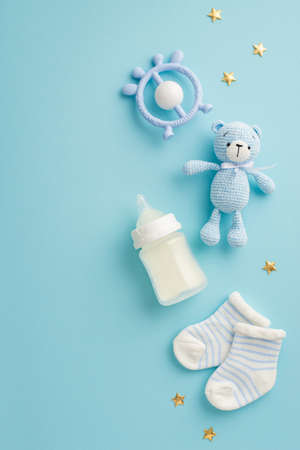 baby accessories concept. Top view vertical photo of socks teether milk bottle knitted teddy-bear toy and gold stars on isolated pastel blue backgroundの写真素材