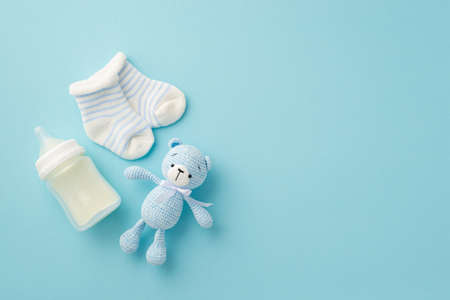 baby boy concept. Top view photo of tiny socks milk bottle and knitted teddy-bear toy on isolated pastel blue backgroundの写真素材