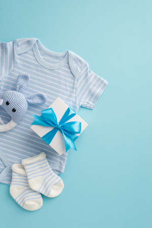 baby accessories concept. Top view vertical photo of bodysuit giftbox socks and knitted bunny rattle toy on isolated pastel blue backgroundの写真素材
