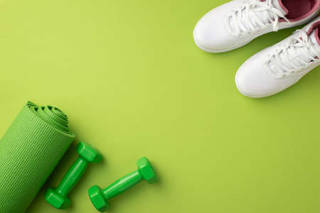 sports concept. Top view photo of white shoes green yoga mat and dumbbells on isolated green...