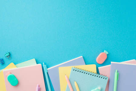 school accessories concept. Top view photo of colorful stationery stacks of notebooks pineapple shaped erasers binder clips and pens on isolated blue background with copyspaceの写真素材