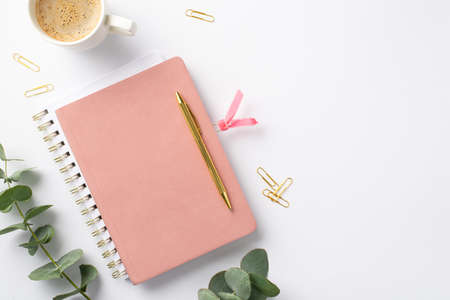 business concept. Top view photo of workplace pink notepad with tab gold pen cup of coffee clips and eucalyptus on isolated white backgroundの写真素材