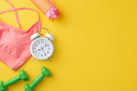 sports concept. Top view photo of pink sports bra bottle of water alarm clock and dumbbells on...