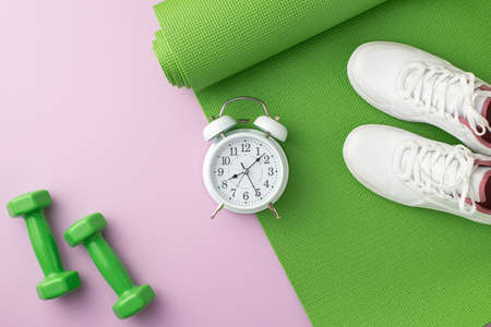 Sports accessories concept. Top view photo of white sneakers over exercise green mat dumbbells and...
