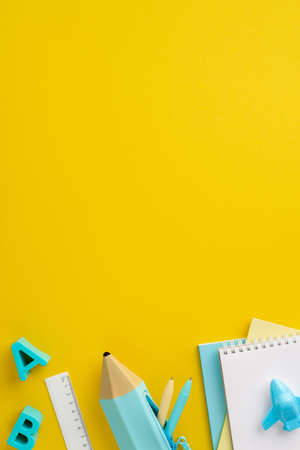 school accessories concept. Top view vertical photo of school supplies plastic alphabet letters notepads pencil-case pens ruler airplane shaped sharpener on isolated yellow background with copyspaceの写真素材